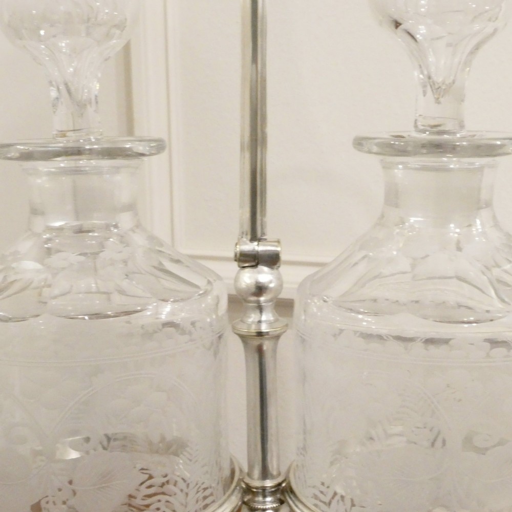 A Victorian silver-plated decanter stand with a central arched handle holding three etched glass decanters with stoppers. View II