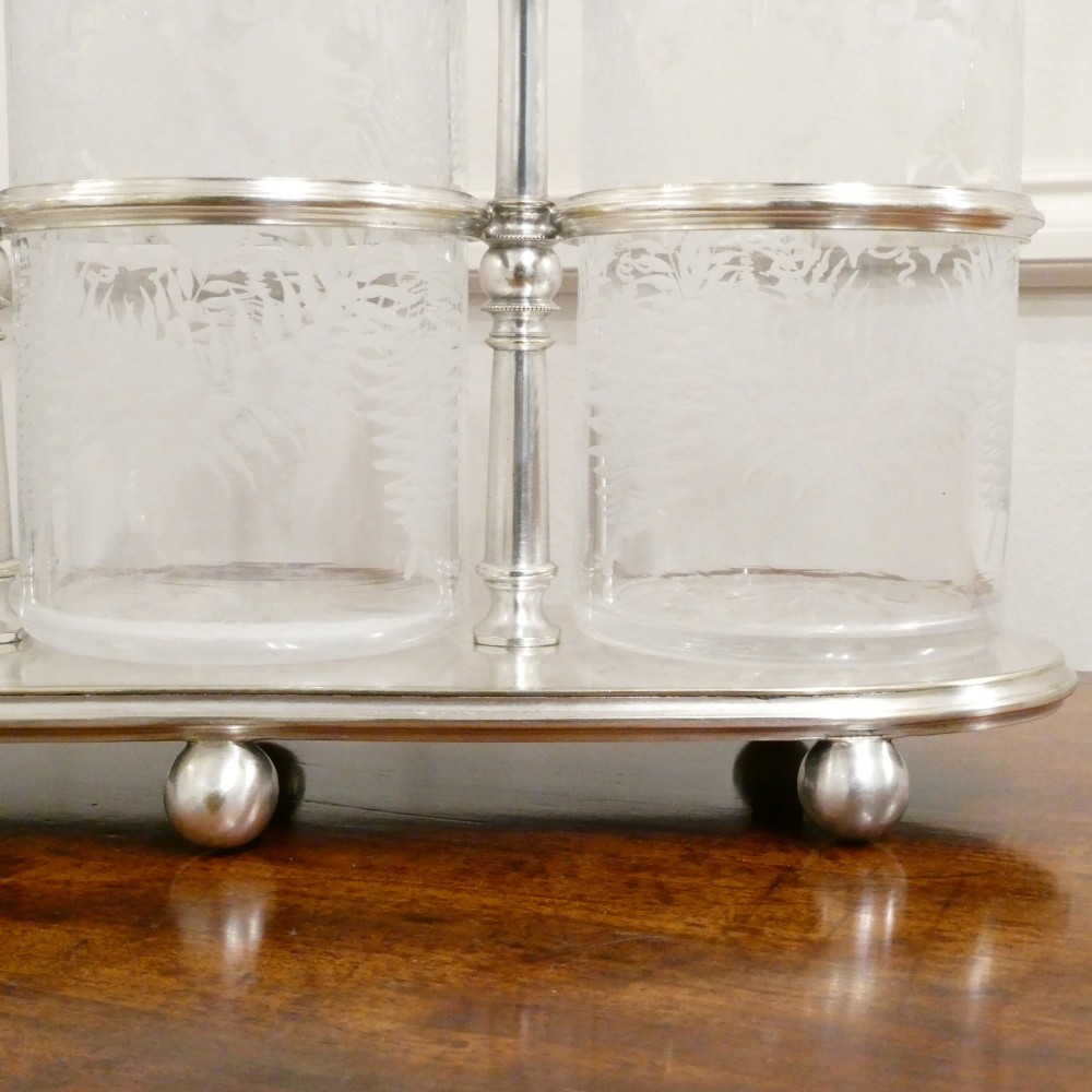 A Victorian silver-plated decanter stand with a central arched handle holding three etched glass decanters with stoppers. View IV