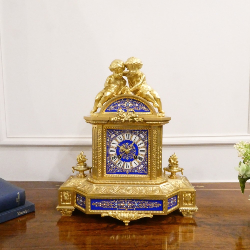 A French gilt bronze mantel clock featuring two cherub figures atop an ornate golden structure with cobalt blue porcelain panels and Roman numerals.