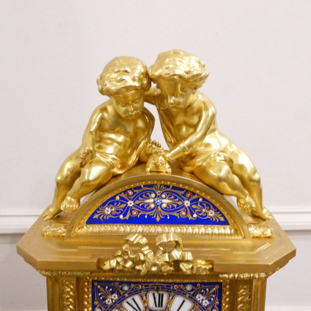 A French gilt bronze mantel clock featuring two cherub figures atop an ornate golden structure with cobalt blue porcelain panels and Roman numerals. View VIII