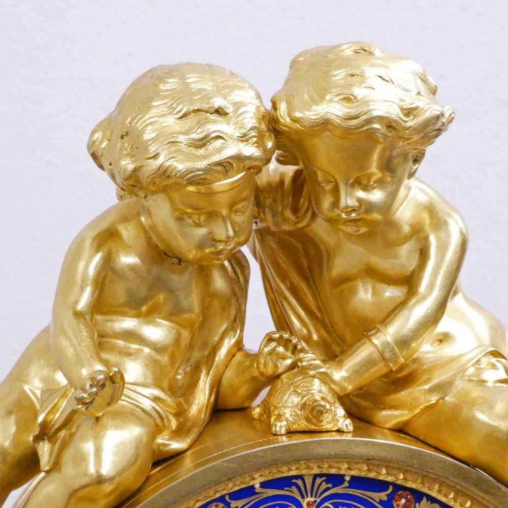 A French gilt bronze mantel clock featuring two cherub figures atop an ornate golden structure with cobalt blue porcelain panels and Roman numerals. View IX