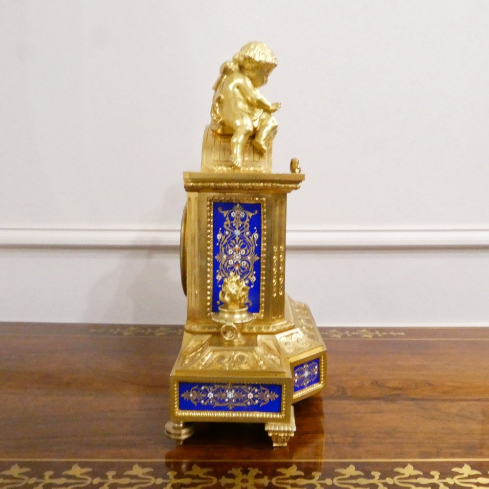 A French gilt bronze mantel clock featuring two cherub figures atop an ornate golden structure with cobalt blue porcelain panels and Roman numerals. View X