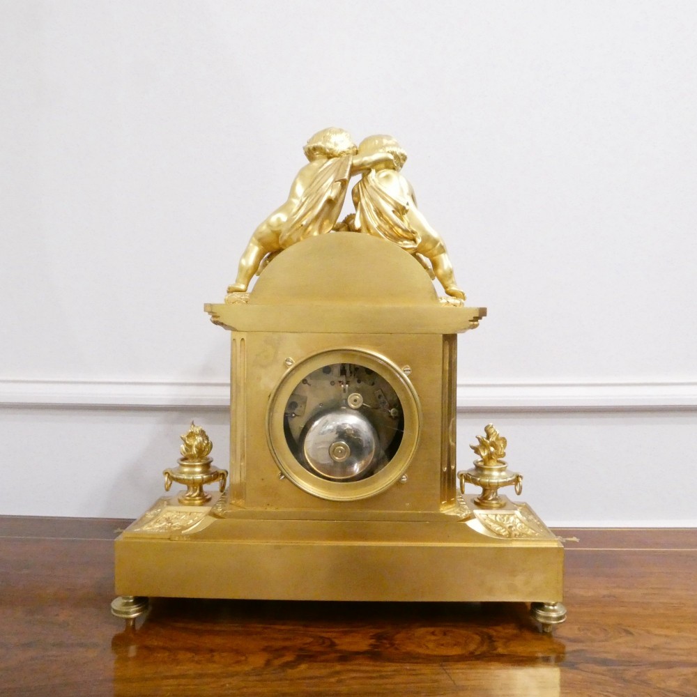 A French gilt bronze mantel clock featuring two cherub figures atop an ornate golden structure with cobalt blue porcelain panels and Roman numerals. View XII