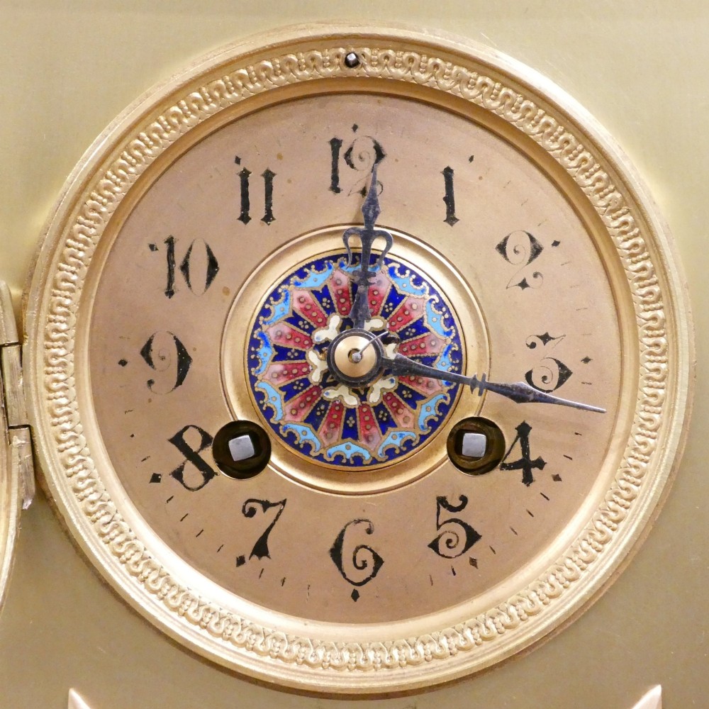 A nineteenth-century French gilt brass mantel clock featuring colourful champleve enamel geometric patterns, flanked by two matching decorative urns. View II