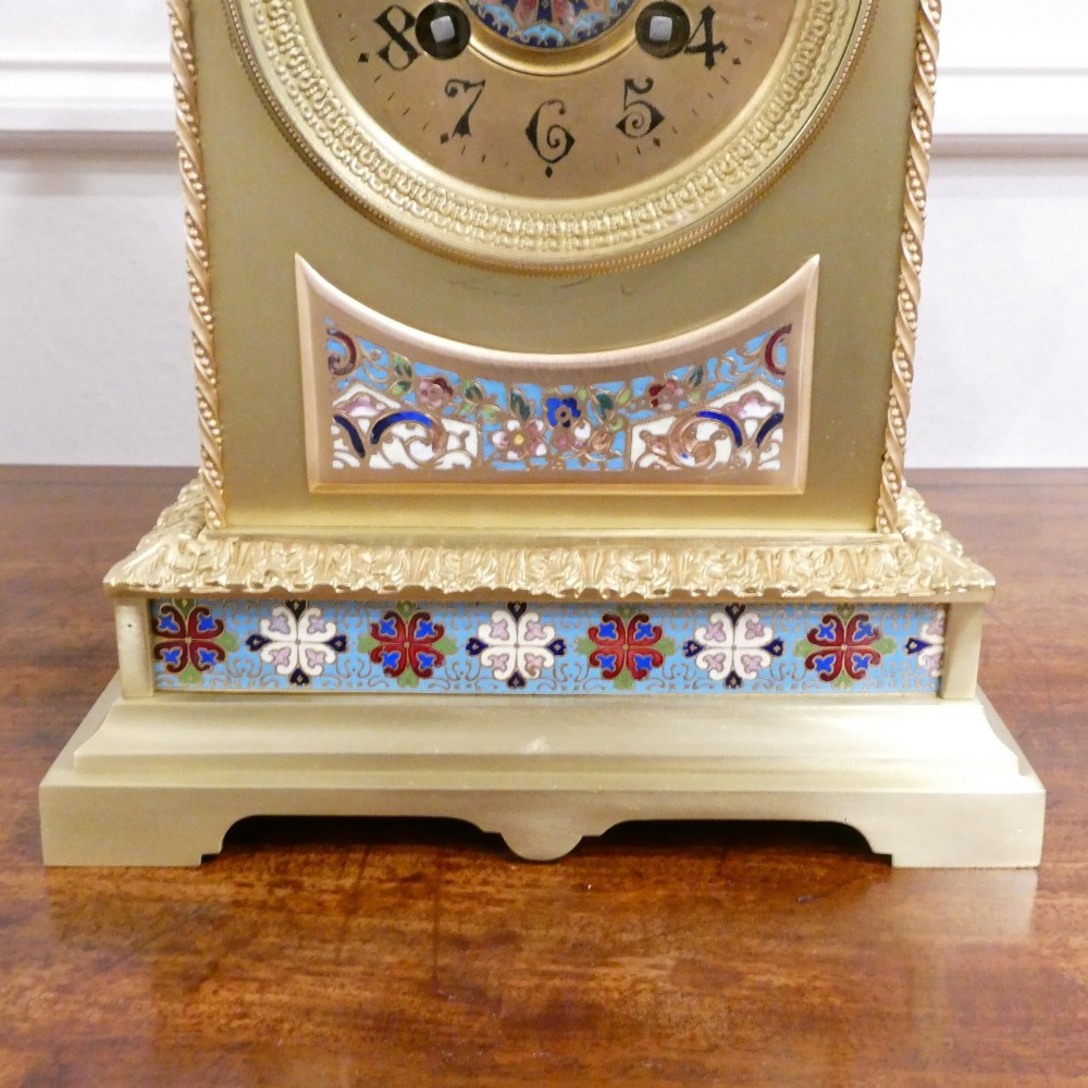 A nineteenth-century French gilt brass mantel clock featuring colourful champleve enamel geometric patterns, flanked by two matching decorative urns. View III