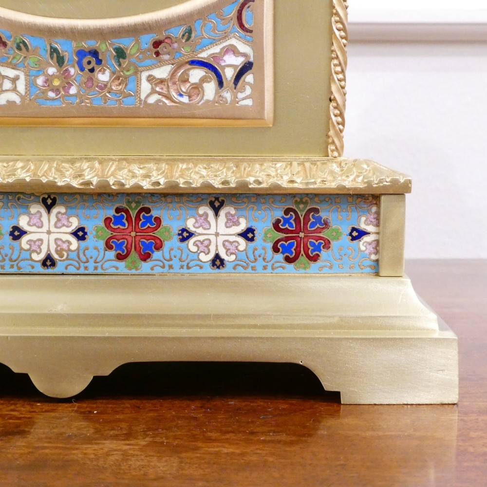 A nineteenth-century French gilt brass mantel clock featuring colourful champleve enamel geometric patterns, flanked by two matching decorative urns. View IV