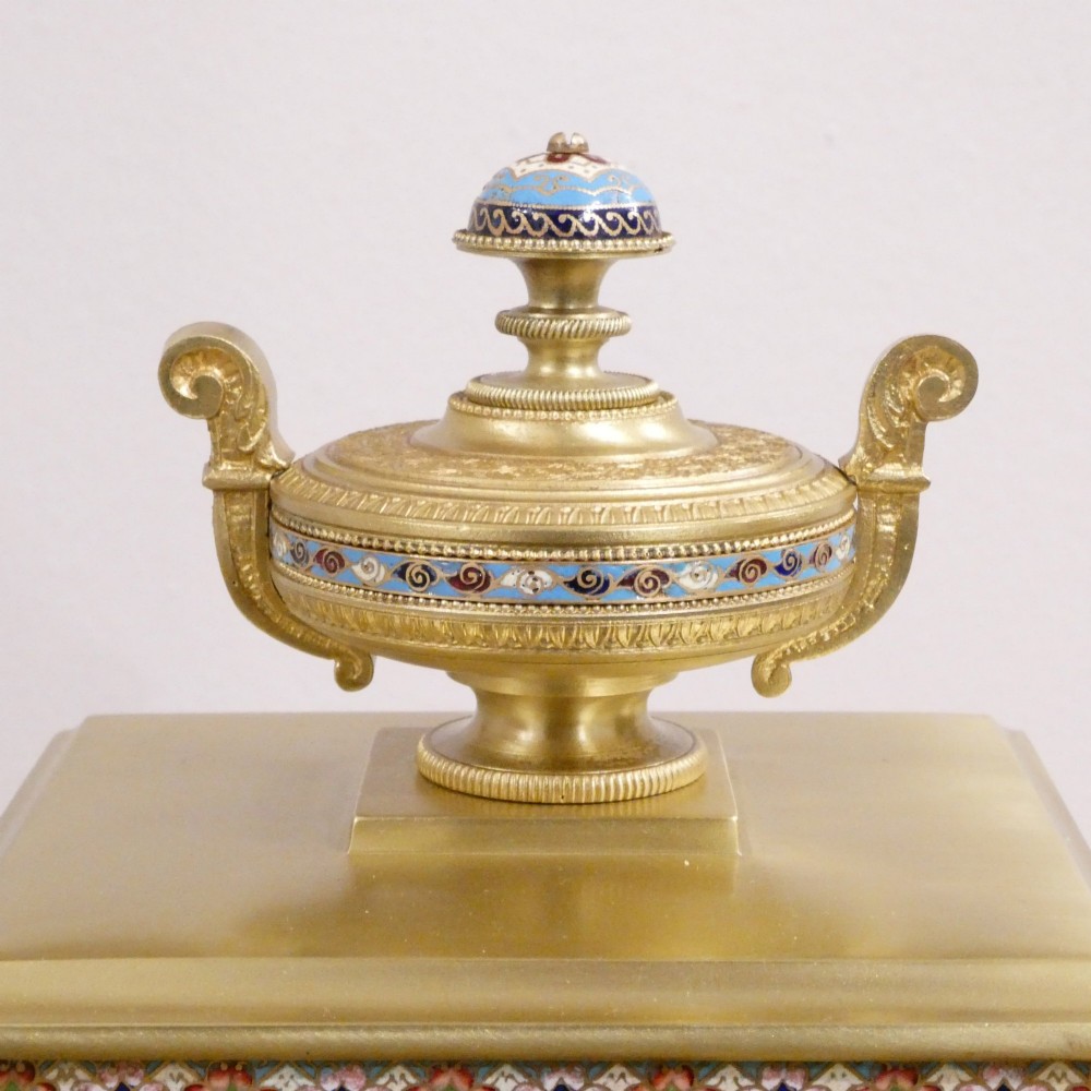 A nineteenth-century French gilt brass mantel clock featuring colourful champleve enamel geometric patterns, flanked by two matching decorative urns. View VI