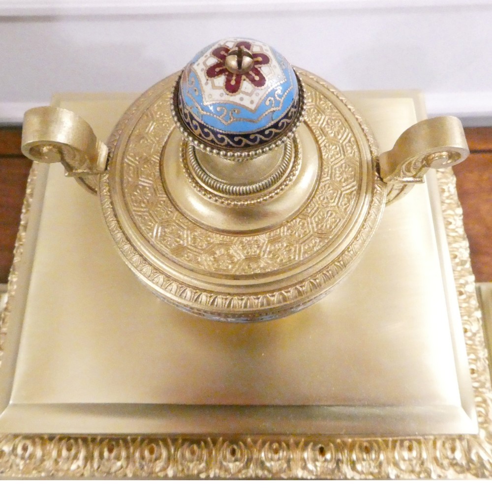 A nineteenth-century French gilt brass mantel clock featuring colourful champleve enamel geometric patterns, flanked by two matching decorative urns. View VII