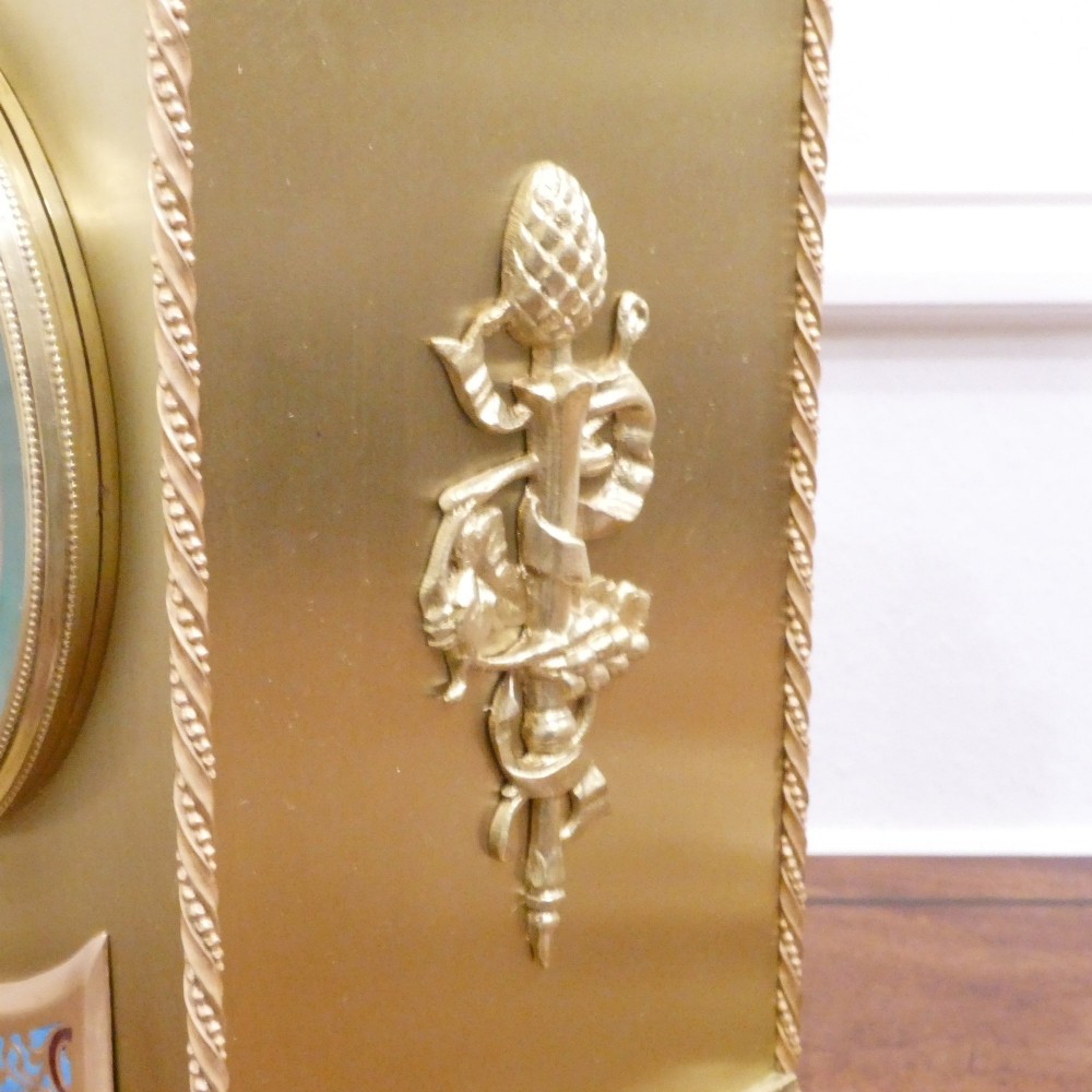 A nineteenth-century French gilt brass mantel clock featuring colourful champleve enamel geometric patterns, flanked by two matching decorative urns. View IX