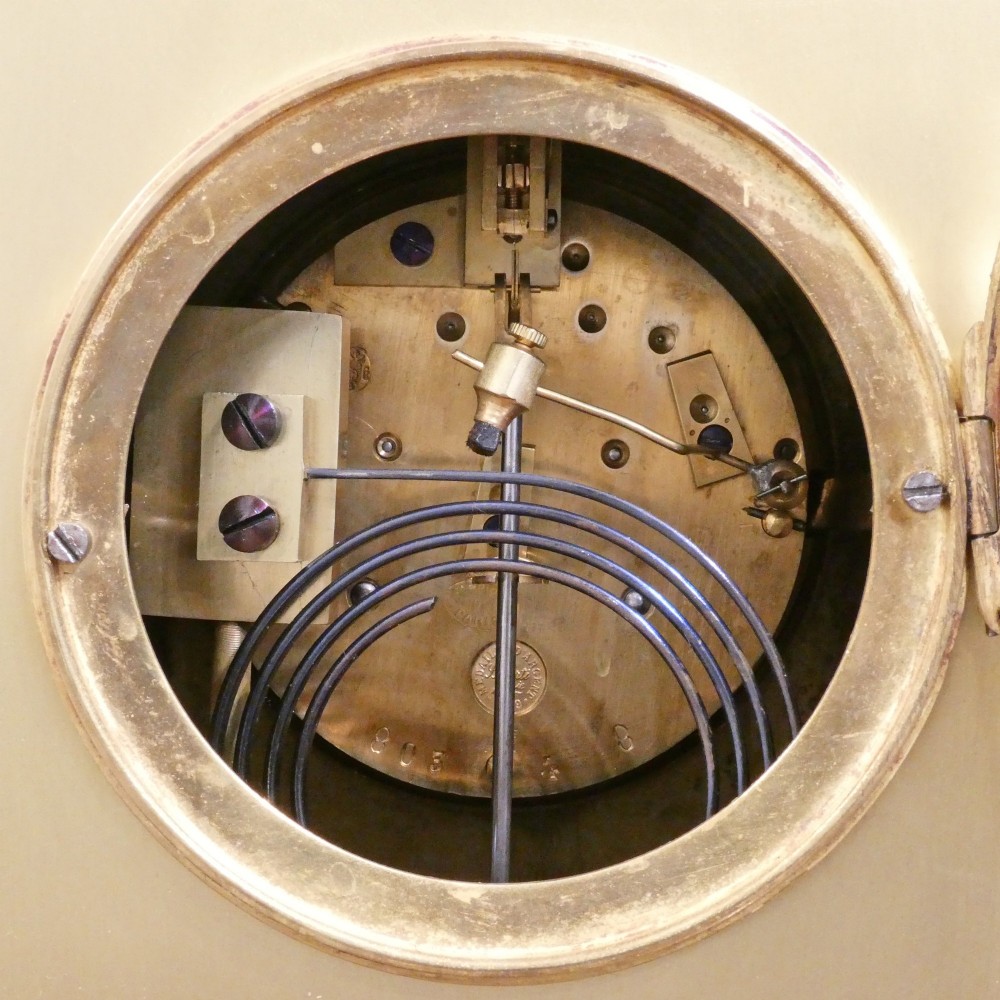 A nineteenth-century French gilt brass mantel clock featuring colourful champleve enamel geometric patterns, flanked by two matching decorative urns. View XI