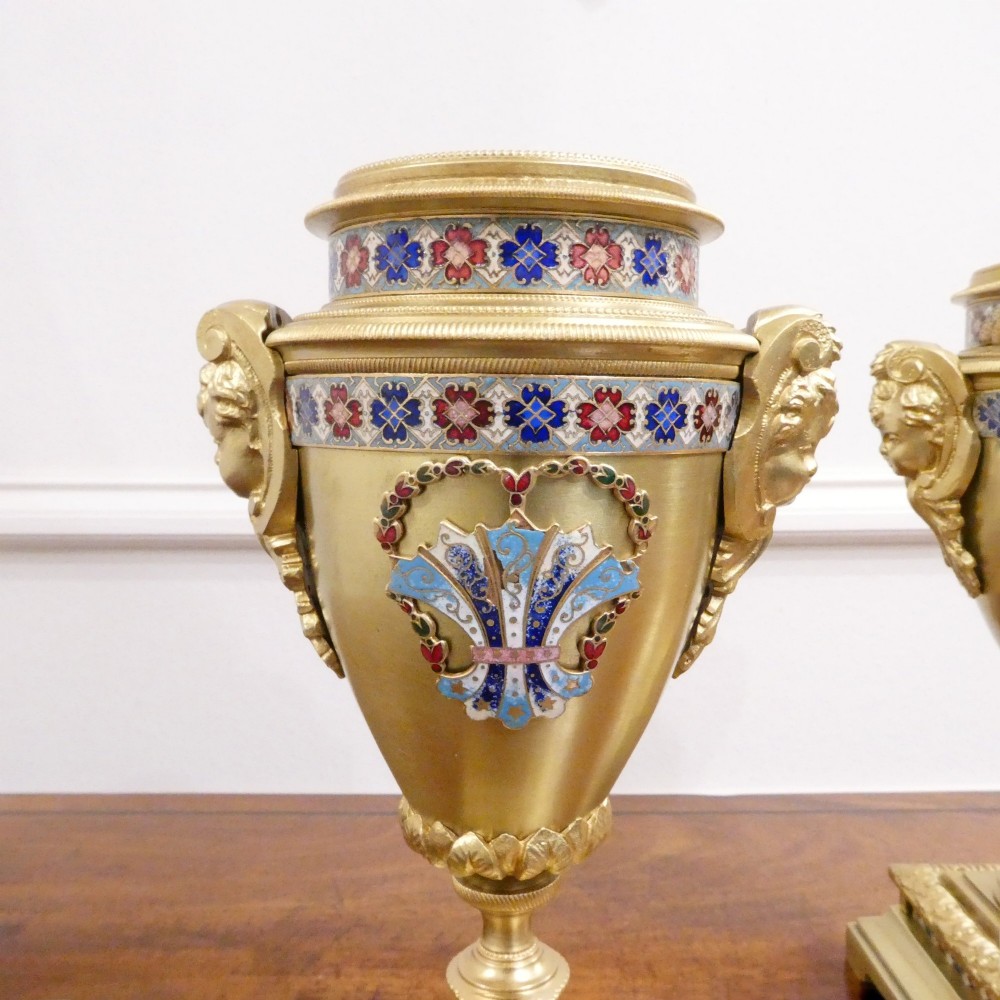A nineteenth-century French gilt brass mantel clock featuring colourful champleve enamel geometric patterns, flanked by two matching decorative urns. View XIII