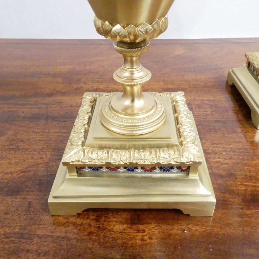 A nineteenth-century French gilt brass mantel clock featuring colourful champleve enamel geometric patterns, flanked by two matching decorative urns. View XIV