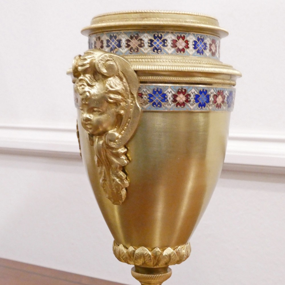 A nineteenth-century French gilt brass mantel clock featuring colourful champleve enamel geometric patterns, flanked by two matching decorative urns. View XV