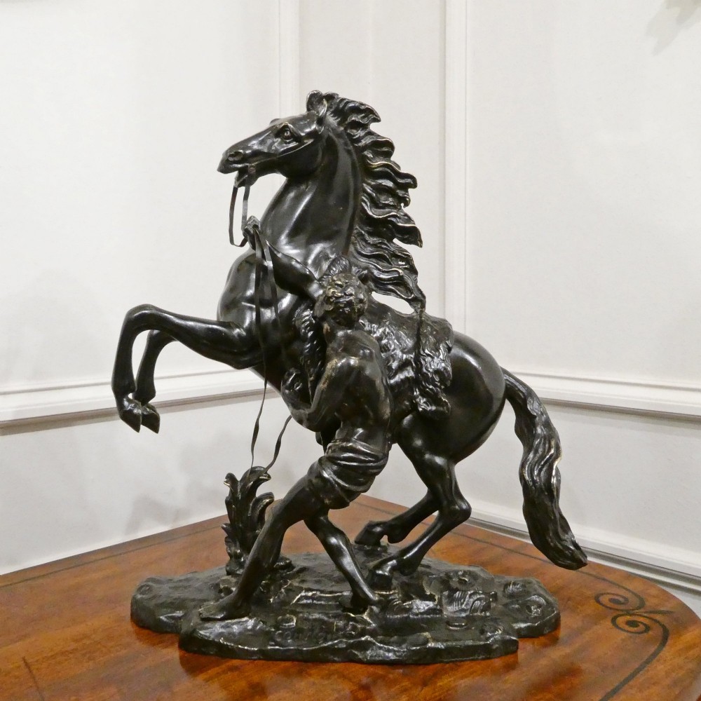 A pair of patinated dark bronze sculptures depicting rearing horses held by grooms on naturalistic bases. View II