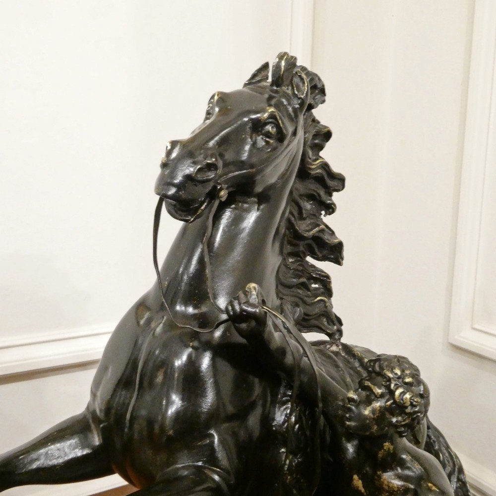 A pair of patinated dark bronze sculptures depicting rearing horses held by grooms on naturalistic bases. View III