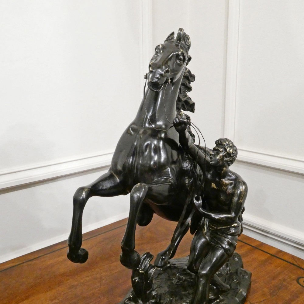A pair of patinated dark bronze sculptures depicting rearing horses held by grooms on naturalistic bases. View IV