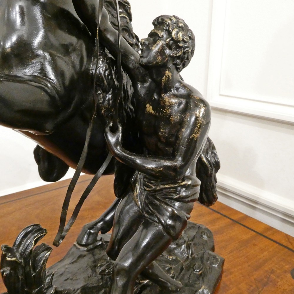 A pair of patinated dark bronze sculptures depicting rearing horses held by grooms on naturalistic bases. View V