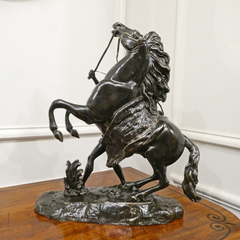 A pair of patinated dark bronze sculptures depicting rearing horses held by grooms on naturalistic bases. View XII