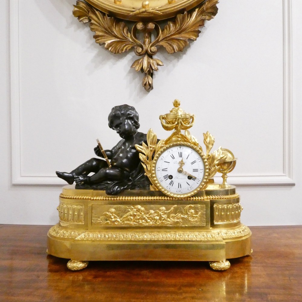 A 19th-century French gilt bronze mantel clock featuring a dark patinated bronze cherub seated beside a circular enamel dial atop a gilt relief base.