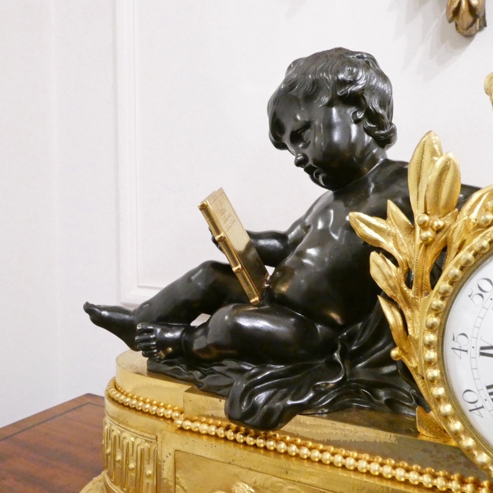 A 19th-century French gilt bronze mantel clock featuring a dark patinated bronze cherub seated beside a circular enamel dial atop a gilt relief base. View V