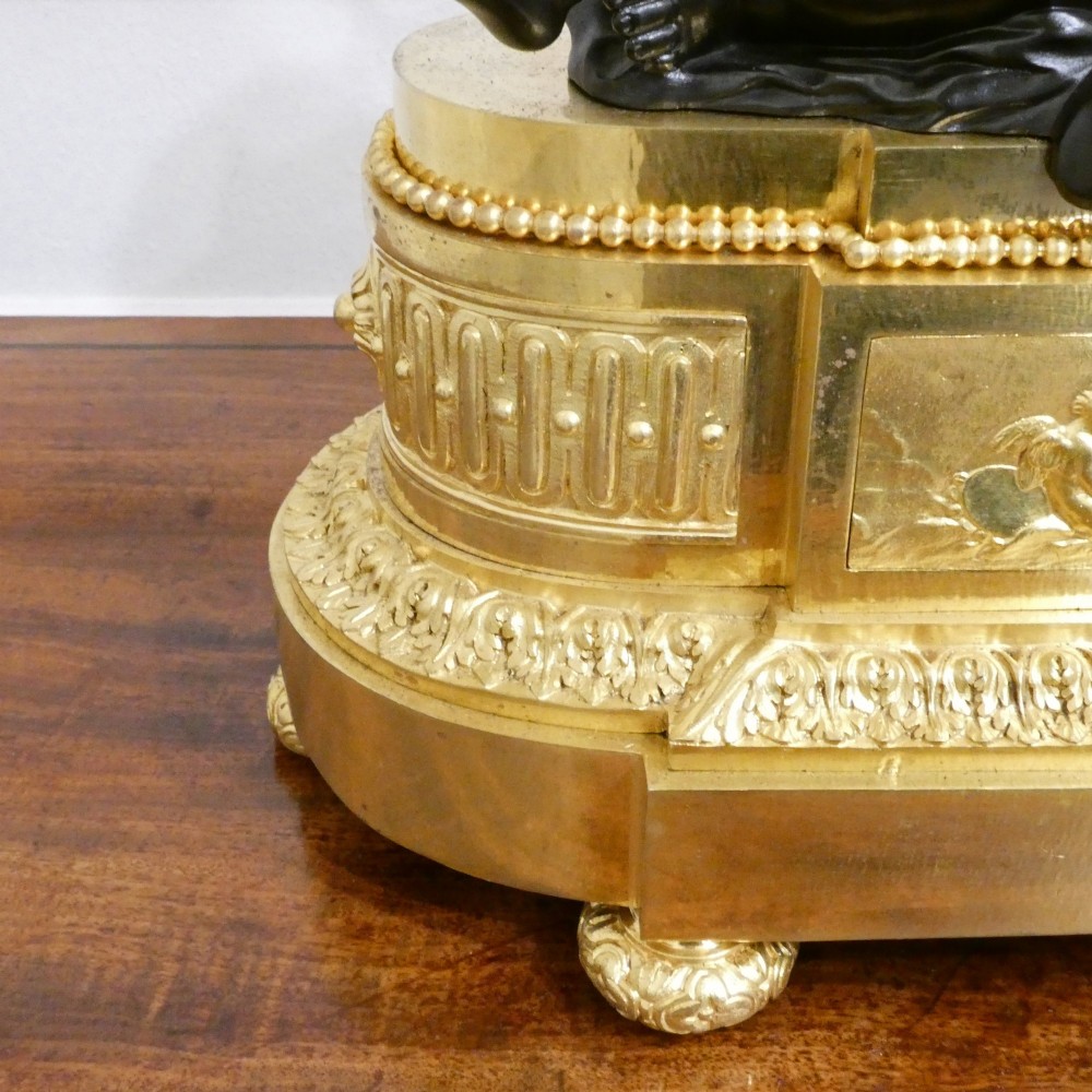 A 19th-century French gilt bronze mantel clock featuring a dark patinated bronze cherub seated beside a circular enamel dial atop a gilt relief base. View VIII