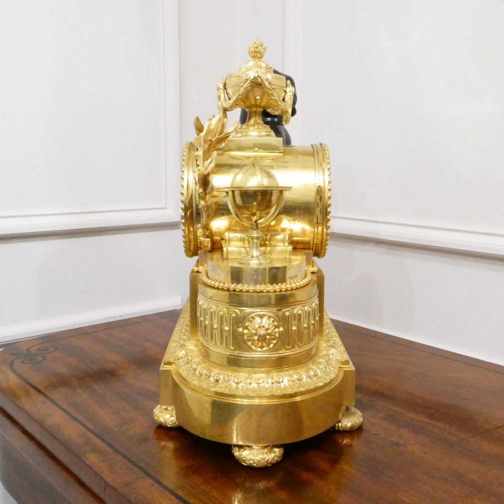 A 19th-century French gilt bronze mantel clock featuring a dark patinated bronze cherub seated beside a circular enamel dial atop a gilt relief base. View XII