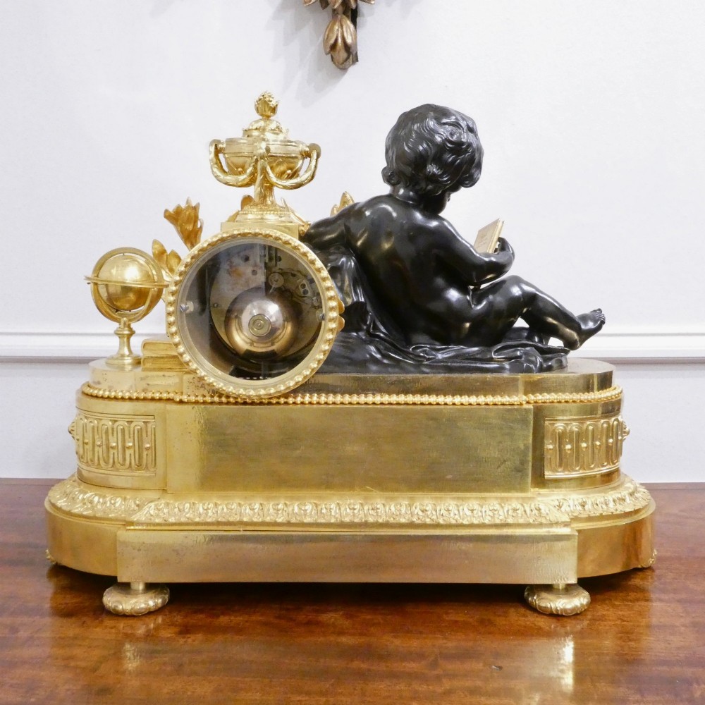 A 19th-century French gilt bronze mantel clock featuring a dark patinated bronze cherub seated beside a circular enamel dial atop a gilt relief base. View XIII