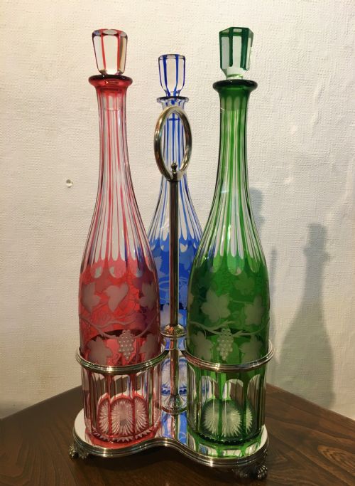 three coloured tall cut vine grape engraved decanters in a handled stand c1840 - CATEGORY: ANTIQUE GLASS - DATED 1850