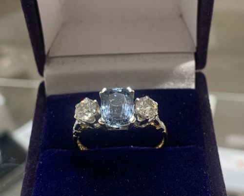 fig 1. An Art Deco trilogy ring featuring a central cushion-cut light blue sapphire flanked by two brilliant-cut diamonds set in platinum claws on an eighteen-carat gold band.