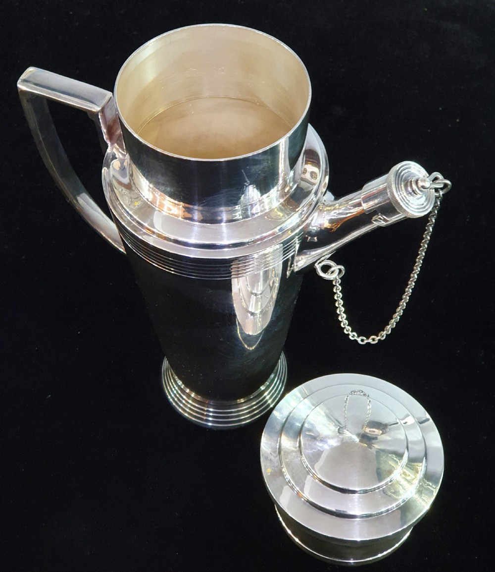 An Art Deco silver-plated cocktail shaker featuring a tapered conical body with turned concentric bands, an angular handle, and a spout with a chained cap stopper. View III