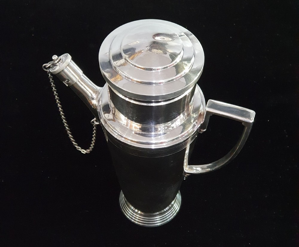 An Art Deco silver-plated cocktail shaker featuring a tapered conical body with turned concentric bands, an angular handle, and a spout with a chained cap stopper. View V