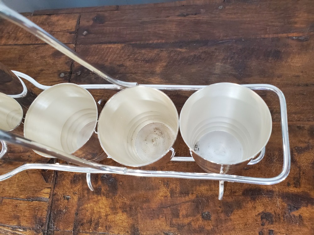 An Art Deco silver-plated cocktail set featuring a central shaker, six matching beakers, and a fitted metal carrying rack with a high arching handle. View III