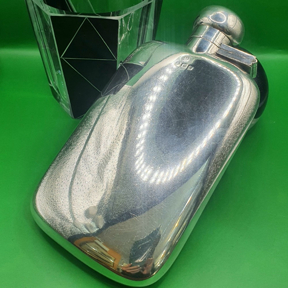 A polished sterling silver hip flask featuring a curved rectangular shape and a hinged bayonet top cap. View VI