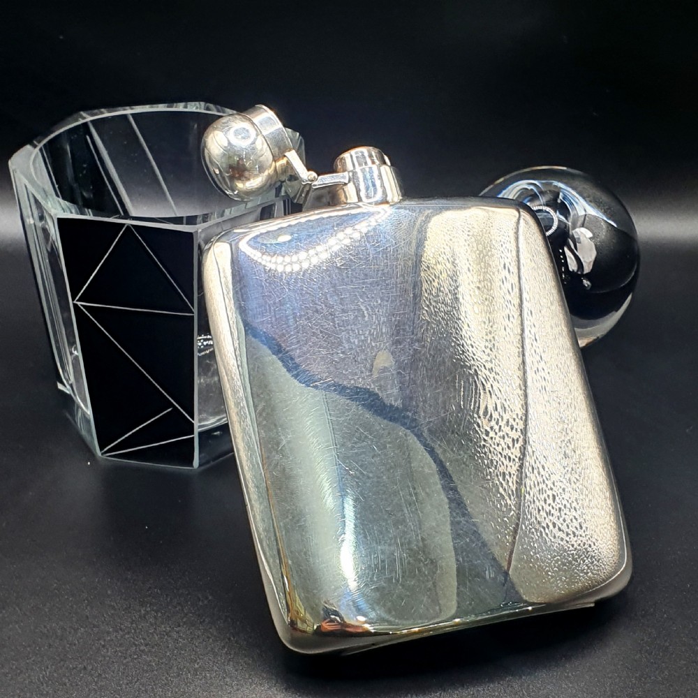 A curved sterling silver hip flask featuring a polished metal surface and a hinged bayonet cap.