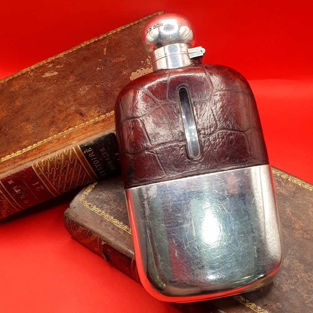 An Edwardian sterling silver hip flask bound in brown crocodile leather featuring a central glass sight window and silver bayonet cap.