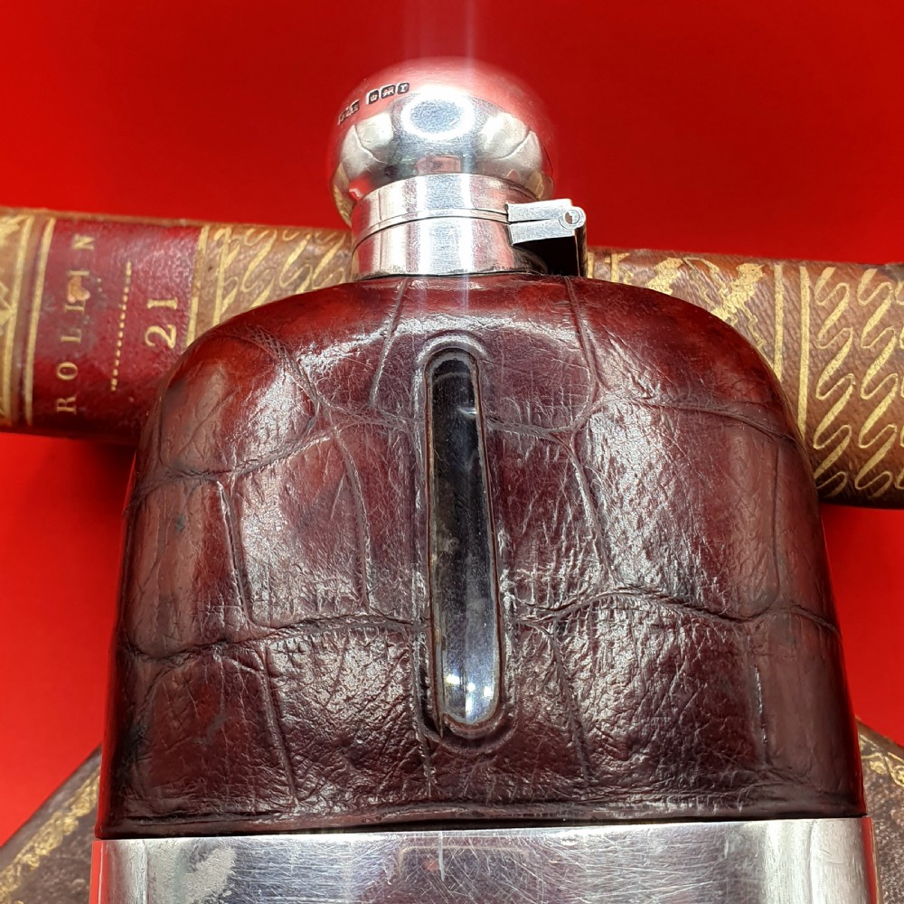 An Edwardian sterling silver hip flask bound in brown crocodile leather featuring a central glass sight window and silver bayonet cap. View II