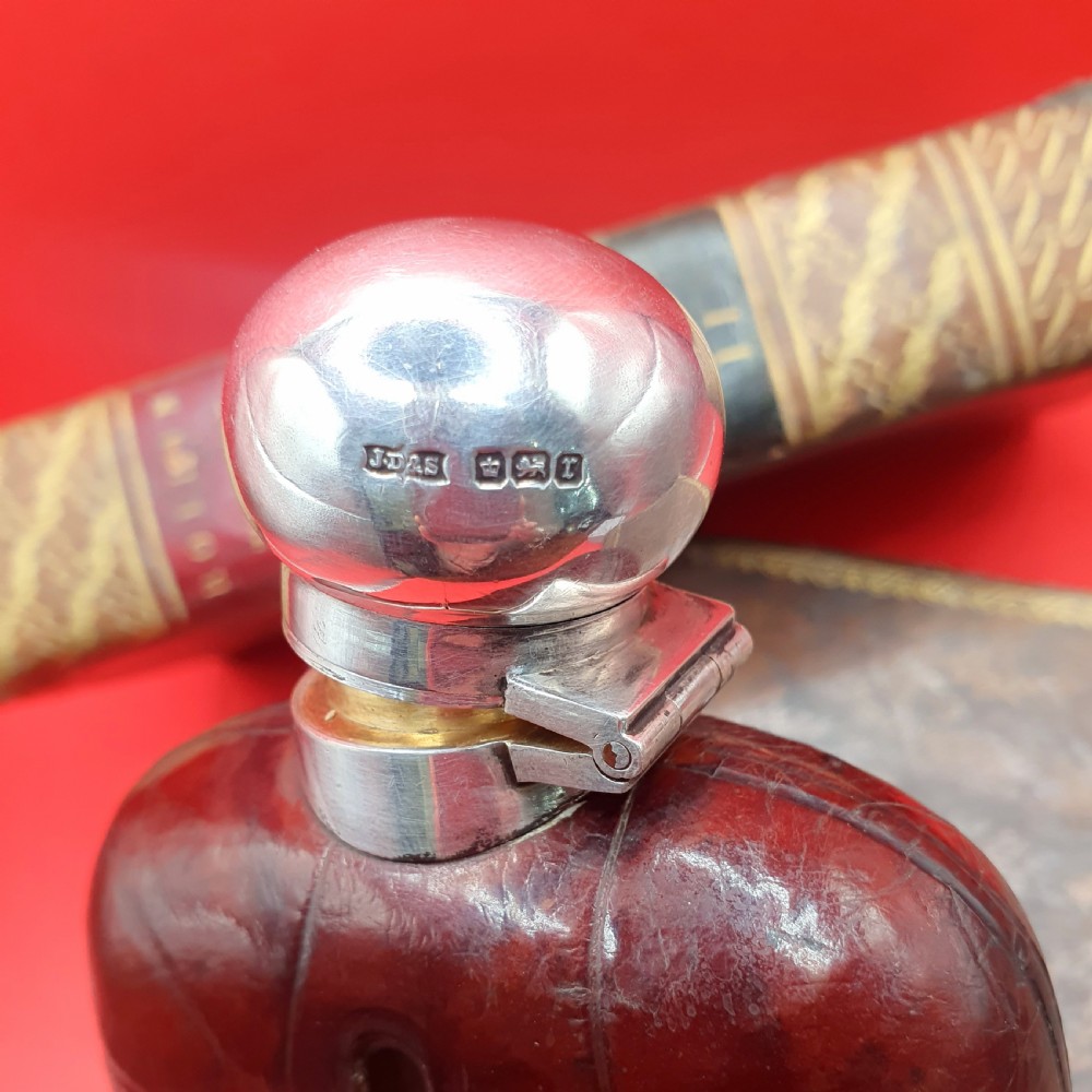 An Edwardian sterling silver hip flask bound in brown crocodile leather featuring a central glass sight window and silver bayonet cap. View VIII