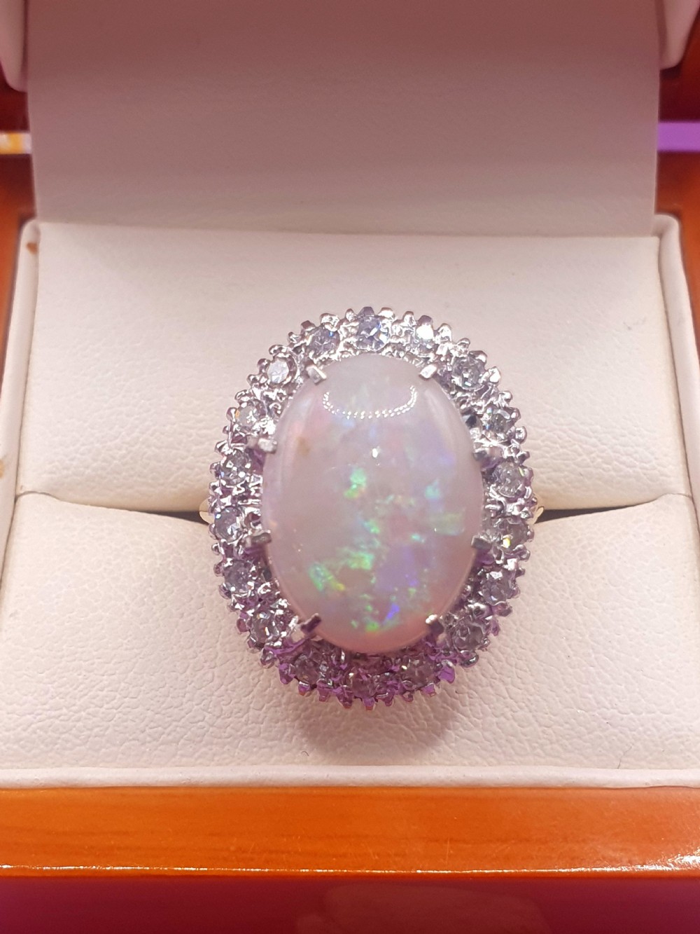 An 18ct gold ring featuring a central oval cabochon opal surrounded by a halo of small diamonds.
