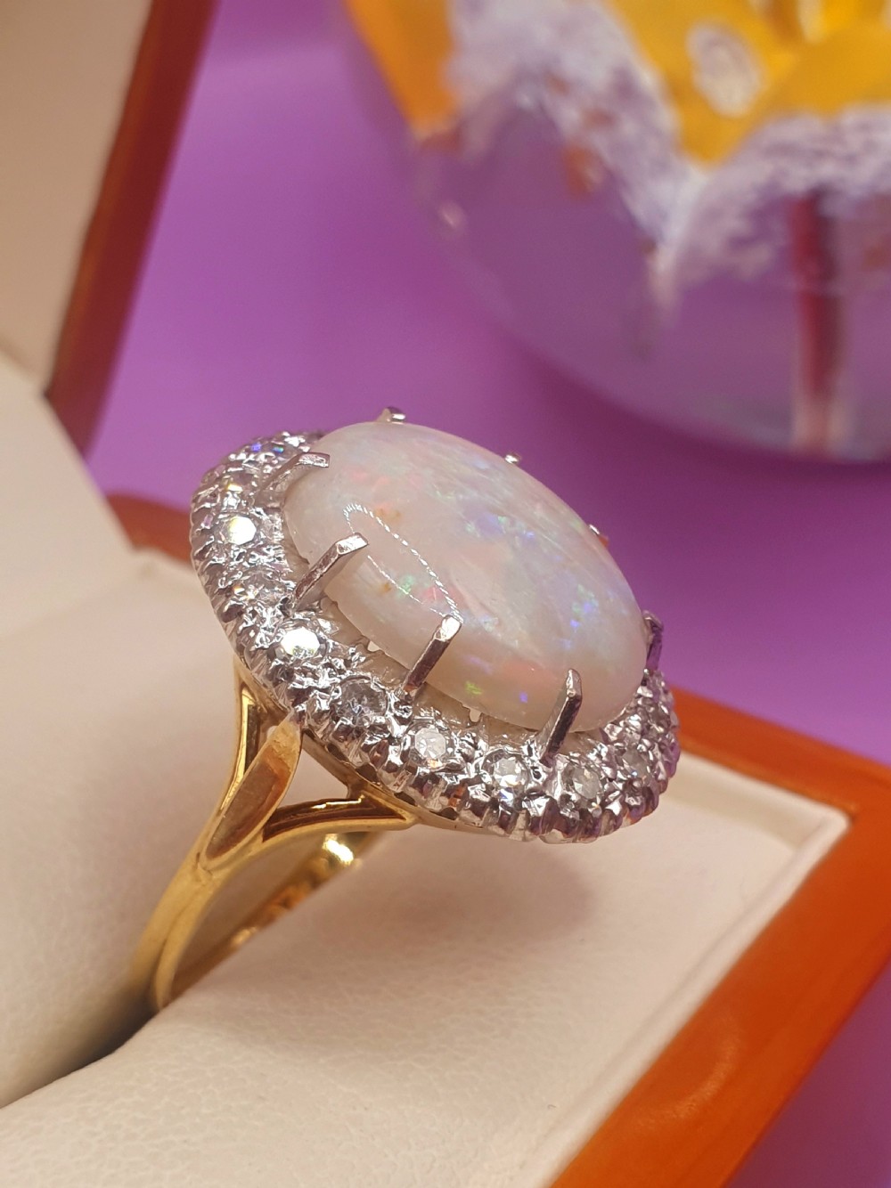An 18ct gold ring featuring a central oval cabochon opal surrounded by a halo of small diamonds. View III