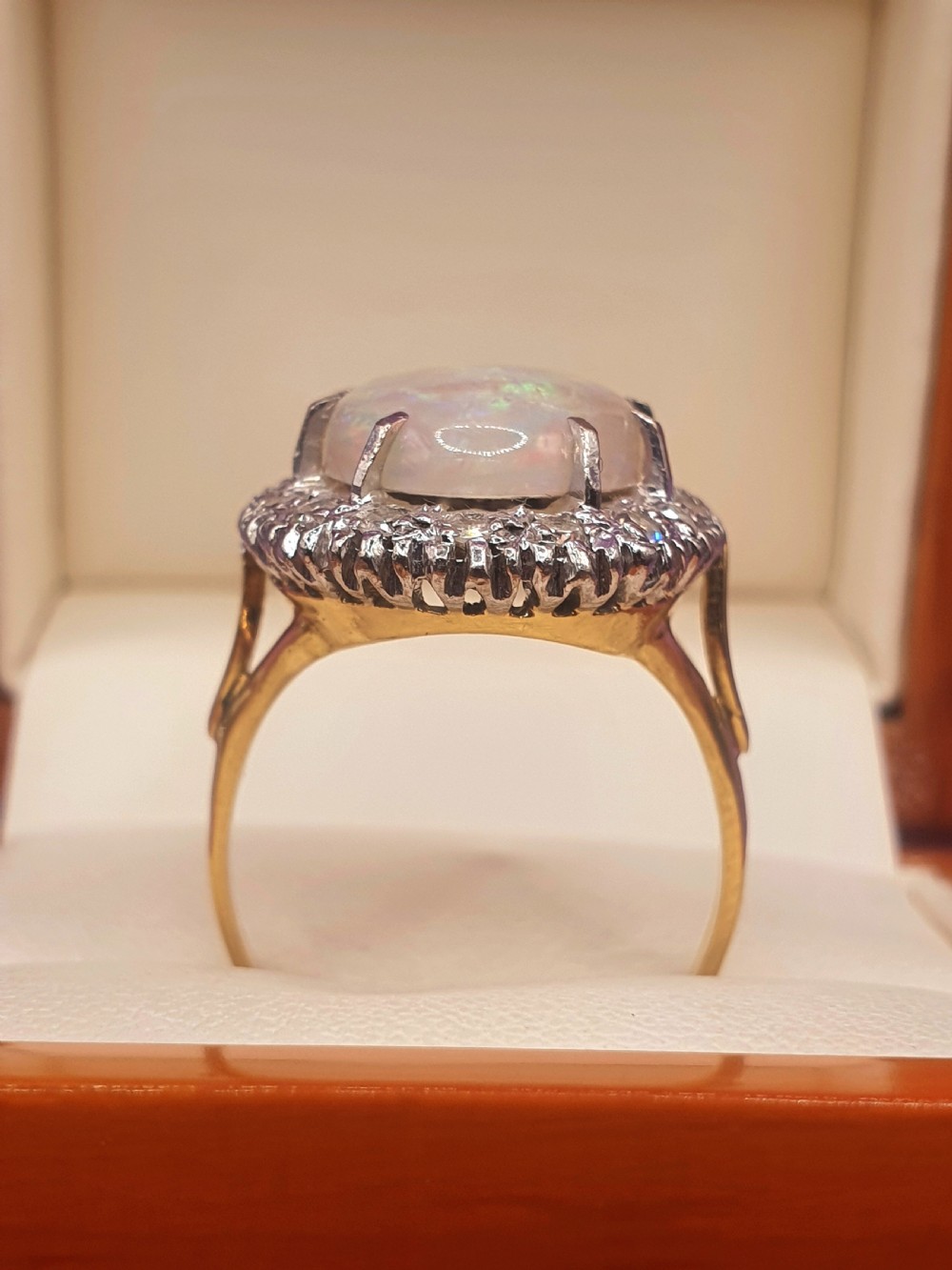 An 18ct gold ring featuring a central oval cabochon opal surrounded by a halo of small diamonds. View IV