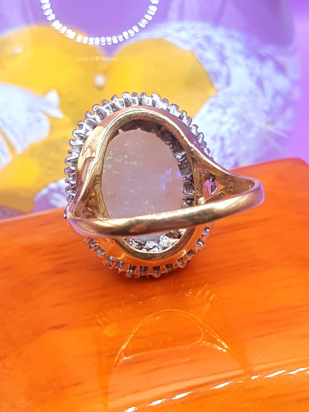An 18ct gold ring featuring a central oval cabochon opal surrounded by a halo of small diamonds. View V