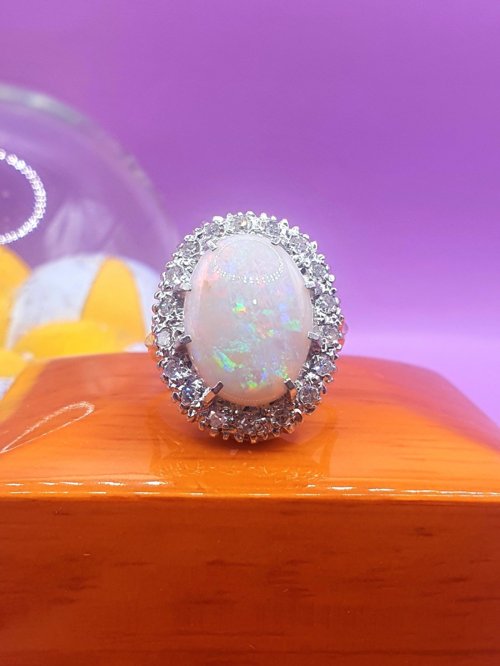 An 18ct gold ring featuring a central oval cabochon opal surrounded by a halo of small diamonds. View VI
