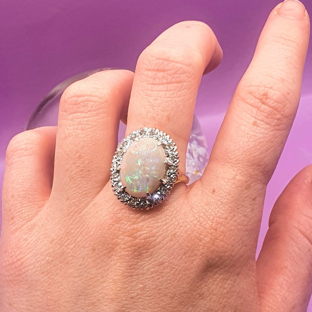 An 18ct gold ring featuring a central oval cabochon opal surrounded by a halo of small diamonds. View VII