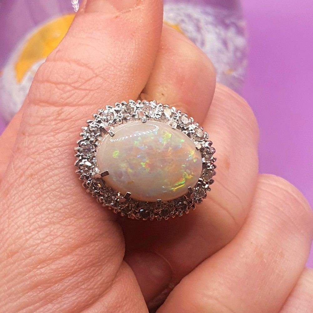 An 18ct gold ring featuring a central oval cabochon opal surrounded by a halo of small diamonds. View VIII