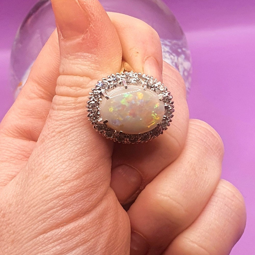 An 18ct gold ring featuring a central oval cabochon opal surrounded by a halo of small diamonds. View IX