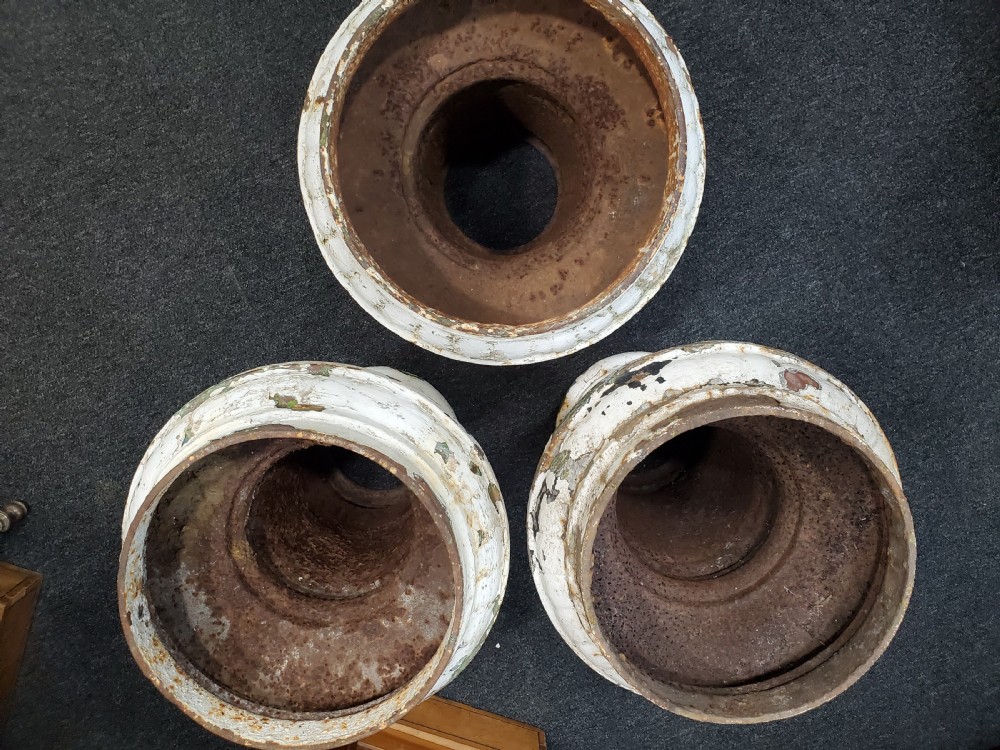 A trio of Victorian cast iron garden urns with fluted pedestals and flanged rims displaying chipped white paint and rust oxidisation. View II