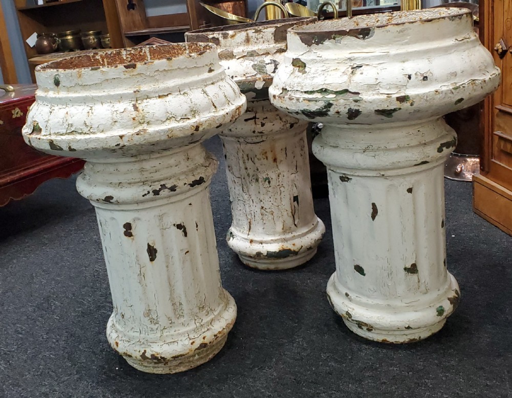 A trio of Victorian cast iron garden urns with fluted pedestals and flanged rims displaying chipped white paint and rust oxidisation. View III