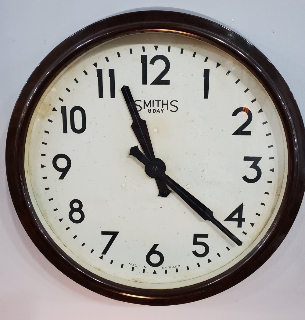 A circular wall clock with a dark brown Bakelite frame, cream dial, bold black numerals, and black clock hands.