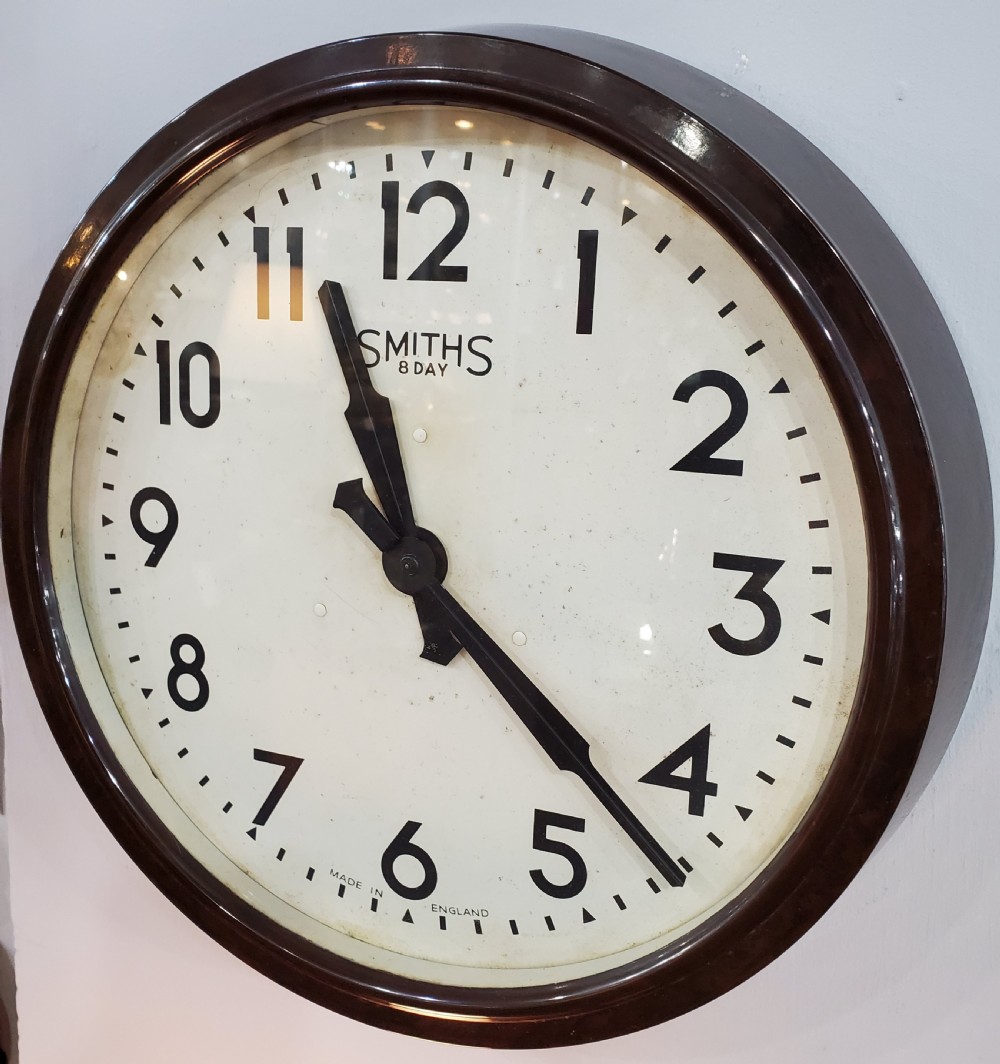 A circular wall clock with a dark brown Bakelite frame, cream dial, bold black numerals, and black clock hands. View III