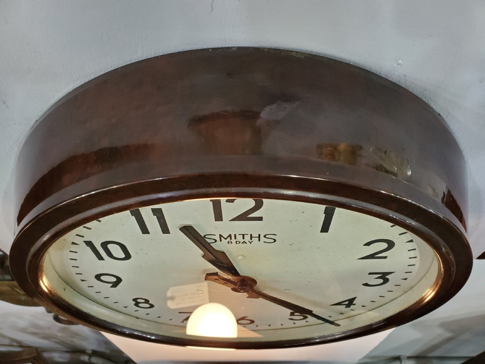 A circular wall clock with a dark brown Bakelite frame, cream dial, bold black numerals, and black clock hands. View IV